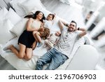 Young parents and their children lie in bed top view. Father, mother and their daughter and newborn son spend the day off at home and have fun in bed. Happy family enjoy spending time with each other