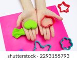 Small photo of The child plays with soft green plasticine and a heart-shaped mold. Hands of a child with airy plasticine and close-up in the shape of a heart. A set of different molds for modeling plasticine