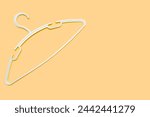 Small photo of Empty plastic hanger isolated on orange background close-up. Potential copy space above and inside clothes hangers. A white clothes hanger is empty without clothes. Potential space for text.