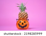 Small photo of Halloween parody funny pineapple in halloween candlestick. Treat dessert fruit for trick or treating, sweetness or nasty. Decoration for all saints day exotic fruits in a scary stand