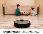 Robot vacuum cleaner is cleaning the floor in the living room and children are playing in the background.
