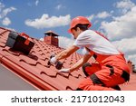 Young man worker master in red overall and helmet is fixing the metal tile roof. 