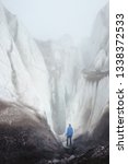 Small photo of A free climber with ice ax stands at foot of Great Glacier next to an epic crack in the fog in the mountains. Insurmountable obstacle