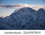 Beautiful mountain peaks in the snow in winter at sunset. Colorful landscape with high snowy cliffs in fog, blue sky with clouds on a cold evening