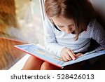 toddler girl with book near the window