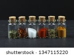 Small photo of Line of small glass vials with cork bungs, filled with a variety of different colored spices on a slate background shot from above