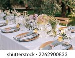 The decor of the wedding dinner in the olive grove. Corner table is decorated with flowers, roses and hydrangeas. Wedding banquet in light white and pink colors
