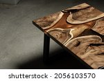 Small photo of Expensive vintage furniture. The table is covered with epoxy resin and varnished. Luxury quality wood processing. Wooden table on a dark background. A gold epoxy river in a round tree slab.