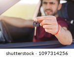 Small photo of Handsome male holds car key while sits in automobile, sells his auto, travells in long journey. Man haulier drives on long distance. Focus on key. Horizontal shot. People and transportation concept