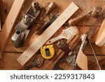 Small photo of Top view of plane, chisel, measure tape, brush on wooden table among the shavings, set of carpentry tools, profession, hobby, carpentry, woodwork, wood carving.