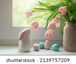 Ceramic Easter bunny, colorful dyed eggs and tulip flowers on windowsill. Decorations for Easter celebration at home. Selective focus.