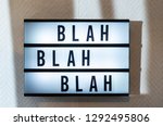 Small photo of Message “blah blah blah” on illuminated board. Boring concept with text. Daylight from window. Room interior. Black letters blah-blah on white wallpaper wall.