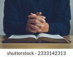 Small photo of Man hands praying to god on the open bible on a wooden table. begging for forgiveness and believing in goodness. Pray for god blessing to wish to have a better life and life to be out of the crisis