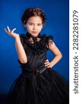 Small photo of Portrait of a little girl in a black dress with a pigtail hairstyle on her head poses, isolated on a dark background with blue backlight.