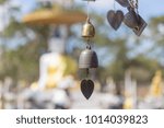 Outdoor zooming closeup view of old vintage rusty rural bell in a heart shape hanging in front of blurred background of white sitting buddha statue in Phu kradueng national park, Loei, Thailand