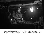 Tired young miner in an old coal mine. A miner in a protective suit with a helmet on his head and a flashlight works in the dark. Work in a coal mine. 