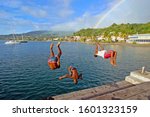 Small photo of Saint-Pierre, Martinique / March-15-2012 : Children playing and jumping from a jetty, with rainbow over city of Saint-Pierre, France's Caribbean overseas department of Martinique