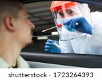 Medical NHS UK worker performing drive-thru COVID-19 check,taking nasal swab specimen sample from male patient through car window,PCR diagnostic for Coronavirus presence,doctor in PPE holding test kit
