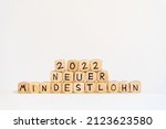 Small photo of 2022 German word for new Minimum wage, NEUER MINDESTLOHN, spelled with wooden letters wooden cube on a plain white background tes, concept image