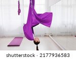 Young girl trainer of aero yoga holding  violet straps in a gym with large windows.  Pretty young woman standing in anti-gravity yoga hall. Mats laying on floor. Stretching and flexibility