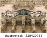 Small photo of Baroque balcony co wrought iron railing and reggi shelf with various stone figures in the baroque style in Modica, Sicily, Italy