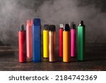 Set of colorful disposable electronic cigarettes on a dark wood background with smoke. The concept of modern smoking, vaping and nicotine.
