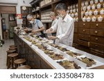 Small photo of Taipei, Taiwan - April 4, 2023: Two men preparing a collection of natural raw herbal ingredients as part of an herbal tonic formula used in Traditional Chinese Medicine (TCM) for cold and flu.