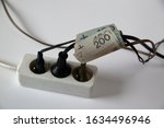 White electric extension cord with three black plugs clsoe up on white background, cables tied with banknotes of 200 and 100 Polish zloty, concept of high costs of electricty