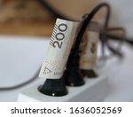 Small photo of 200 Polish zloty banknote between wires of plugs in electric extension cord close up on concept of costs of electricty / recompense of high costs of energy