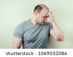 Small photo of a portrait of a bald man is sad against a gray background. problem of male pattern baldness. sadness, vexation and anger