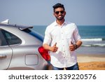 Indian businessman standing near car outdoors on sea beach summer good day.a man in a white shirt and snow-white smile rejoicing buying a new car enjoying a vacation by the ocean
