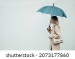 Young smiling businesswoman with umbrella and shoulder bag walking down city street during rain