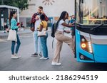 Multiracial passengers waiting at a bus stop and talking cheerfully. Focus on an african american woman entering the bus. Diverse tourists in new town. Best friends traveling together in a city.