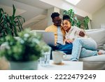 Small photo of Diverse young relaxed couple using laptop while watching funny movie or enjoying comedian film and hugging at home on the sofa. Shopping online or web surfing. Multiracial couple spending time at home