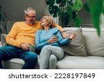 Small photo of Portrait of a happy elderly couple hugging and relaxing together on the sofa at home and drinking coffee. Senior couple having a conversation together while relaxing on the couch. Copy space.