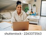 Small photo of Portrait of a hispanic woman looking into laptop and planning future while making a financial plan. Online banking, paying rant and bills. Looking into the camera and smiling.