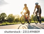 Small photo of Portrait of a couple of athletes dressed in activewear biking on paved road. Countryside area, sunny day outdoors. Professional road bicycle racers in action while riding outside of the city.