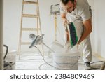A constructor is standing in a house in a renovation process, adding plaster into a bucket and making skim coating paste. A builder pouring plaster in a bucket and preparing material for plastering.