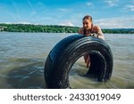 Small photo of Strong woman athlete partake in one of the events of an obstacle course race while pushing tractor tire in a water. Female working out outside. Sport competition and OCR race.