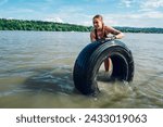 Small photo of Portrait of a smiling woman athlete partake in one of the events of an obstacle course race while pushing a tractor tire in a shallow water. Female working out outside. Sport competition and OCR race.