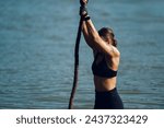 Small photo of Woman athlete partake in one of the events of an obstacle course race while preparing to climb the rope. Female working out outside. Sport competition and OCR race. Copy space.