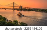 Small photo of Artistic view of evening in Savannah, Georgia, as tourists gather on the river bank and a tug boat makes a wake heading into the golden sky under the Talmadge Memorial Bridge.