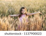 Small photo of Smiling girl in pink dress on yellow wheat ears field with sunlights on face and throw open hands