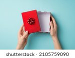 Small photo of First person top view photo of valentine's day decorations woman's hands opening giftbox with red lid and star bow on isolated pastel blue background with empty space