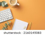 Business concept. Top view photo of workplace white keyboard organizer gold pen clips cup of coffee on rattan serving mat and eucalyptus leaves on isolated orange background with copyspace