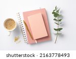 Business concept. Top view photo of workplace stack of pink diaries cup of coffee clips gold pen and eucalyptus sprig on isolated white background