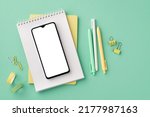 Back to school concept. Top view photo of school supplies smartphone on notepad pens binder clips and adhesive tape on isolated pastel green background with copyspace