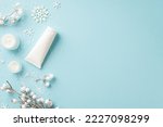 Small photo of Winter skin care cosmetics concept. Top view photo of jars of cream white tube of lotion without label snowflakes sow and plant branches in frost on isolated light blue background with empty space