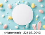 Easter decorations concept. Top view photo of white circle colorful easter eggs bunny ears and sprinkles on isolated light blue background with copyspace