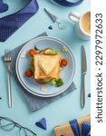 Small photo of Treat Dad to a breakfast surprise on Father's Day. Top view vertical photo of a homemade sandwich, heart-shaped cheese, cutlery, coffee, napkin, giftbox, men's accessories, on a pastel blue background